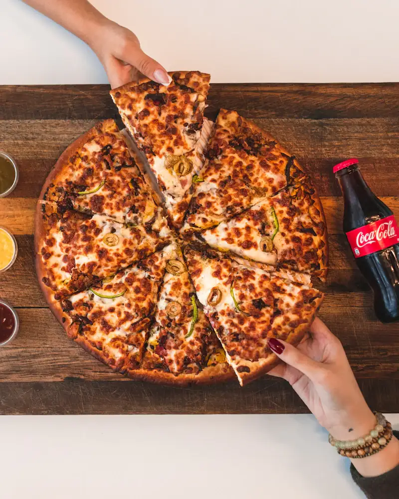 Dos manos cogiendo porciones de una pizza sobre una tabla de madera